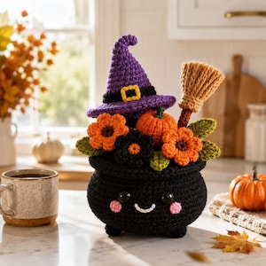 May include: A crocheted black cauldron with a smiling face, pink cheeks, and black eyes. It is filled with orange and black crocheted flowers, green leaves, a small orange pumpkin, a tan broom, and a purple witch hat with a black and yellow band.