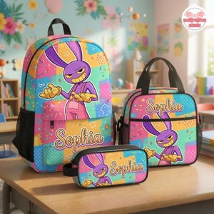 May include: A backpack, lunch bag, and pencil case set featuring a purple cartoon rabbit character on a colorful geometric background. Each item displays the name Sophia in a cursive font. The design includes pink, blue, and yellow patterns.