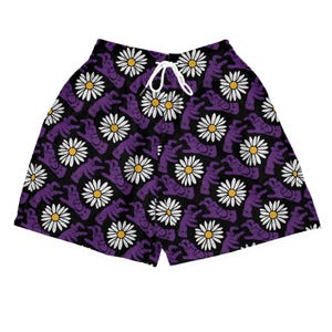 Könnte beinhalten: Schwarze Shorts mit einem sich wiederholenden Muster aus lila Händen und weißen Gänseblümchen mit gelben Zentren. Die Shorts haben einen weißen Kordelzug und sind aus leichtem Stoff gefertigt.