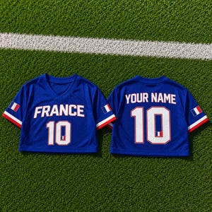 May include: Two blue mesh crop tops with white lettering and the number 10. One top says "FRANCE" and the other says "YOUR NAME". Each has a French flag on the sleeve and is on a green surface.