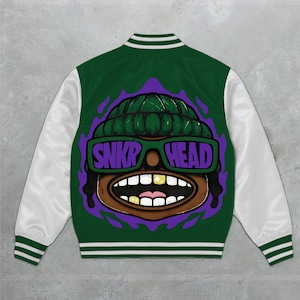 May include: A dark green varsity jacket with white sleeves and striped ribbed trim. The back features a graphic of a character wearing a green beanie and green sunglasses with the text SNKR HEAD, showing a wide mouth with gold teeth.