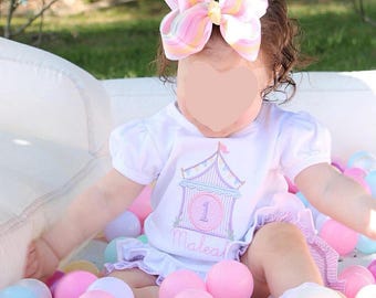 Peut inclure: Un t-shirt blanc à manches courtes avec un ourlet à volants et un motif de chapiteau de cirque aux tons pastel, incluant le chiffre 1 et le prénom Maleah. Un grand nœud pour cheveux à rayures pastel est porté, assorti au motif du t-shirt.