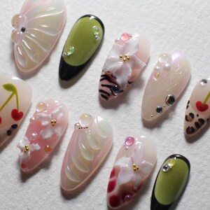 May include: A collection of artificial nails with various designs. Some nails feature 3D floral embellishments, while others have cherry, leopard print, or abstract patterns. Colors include pink, white, green, and black, with iridescent and glitter accents.