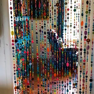 Pu&ograve; includere: Una tenda per porta fatta di perline colorate di varie forme e dimensioni. Le perline sono infilate in file verticali, creando uno schermo decorativo vibrante. La tavolozza dei colori comprende rosso, arancione, giallo, verde, blu e viola.
