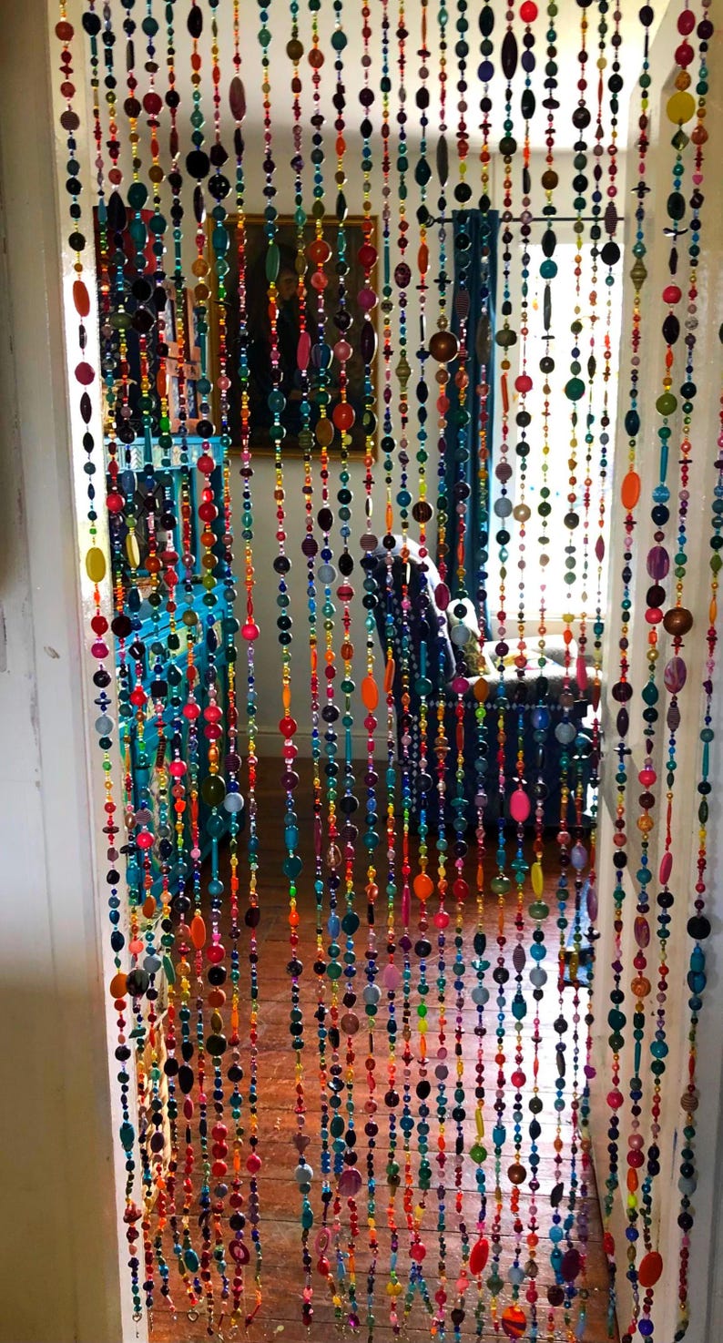 Pu&ograve; includere: Una tenda per porta fatta di perline colorate di varie forme e dimensioni. Le perline sono infilate in file verticali, creando uno schermo decorativo vibrante. La tavolozza dei colori comprende rosso, arancione, giallo, verde, blu e viola.