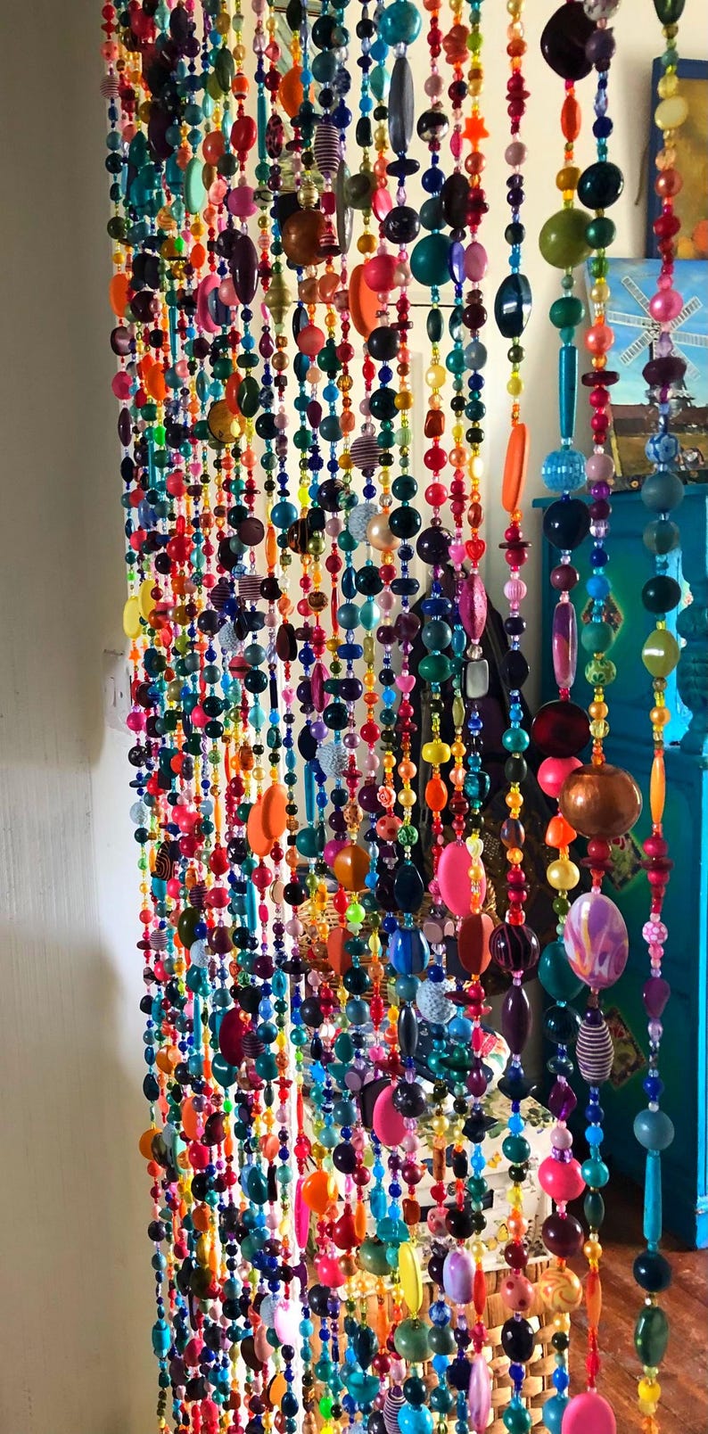 Pu&ograve; includere: Una vivace tenda di perline con fili di perline colorate di varie forme e dimensioni. Le perline sono nelle tonalit&agrave; di rosso, arancione, giallo, verde, blu, viola e rosa. La tenda &egrave; appesa davanti a un muro bianco.