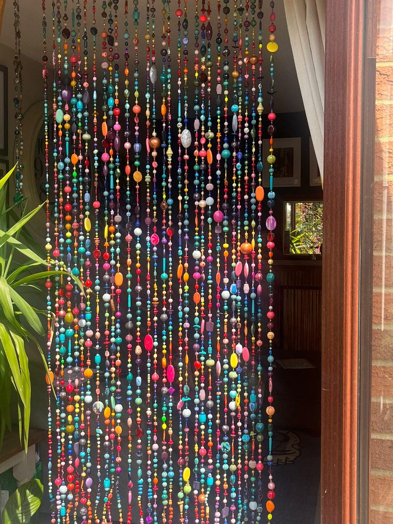 Pu&ograve; includere: Una tenda di perline con una vibrante gamma di colori, tra cui rosso, arancione, giallo, verde, blu e viola. Le perline sono di varie forme e dimensioni, creando un accento decorativo e accattivante per la porta.