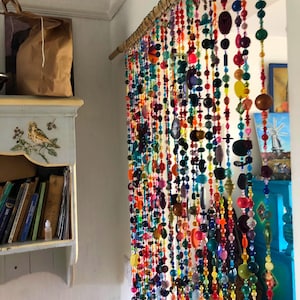 Pu&ograve; includere: Una colorata tenda di perline &egrave; appesa in una porta, con perline di varie forme e dimensioni. Le perline sono infilate in fili verticali. I colori includono rosso, arancione, giallo, verde, blu e viola, creando un elemento decorativo vivace.