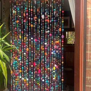 Pu&ograve; includere: Una tenda di perline con una vibrante gamma di colori, tra cui rosso, arancione, giallo, verde, blu e viola. Le perline sono di varie forme e dimensioni, creando un design strutturato e visivamente accattivante. La tenda &egrave; appesa in una porta.