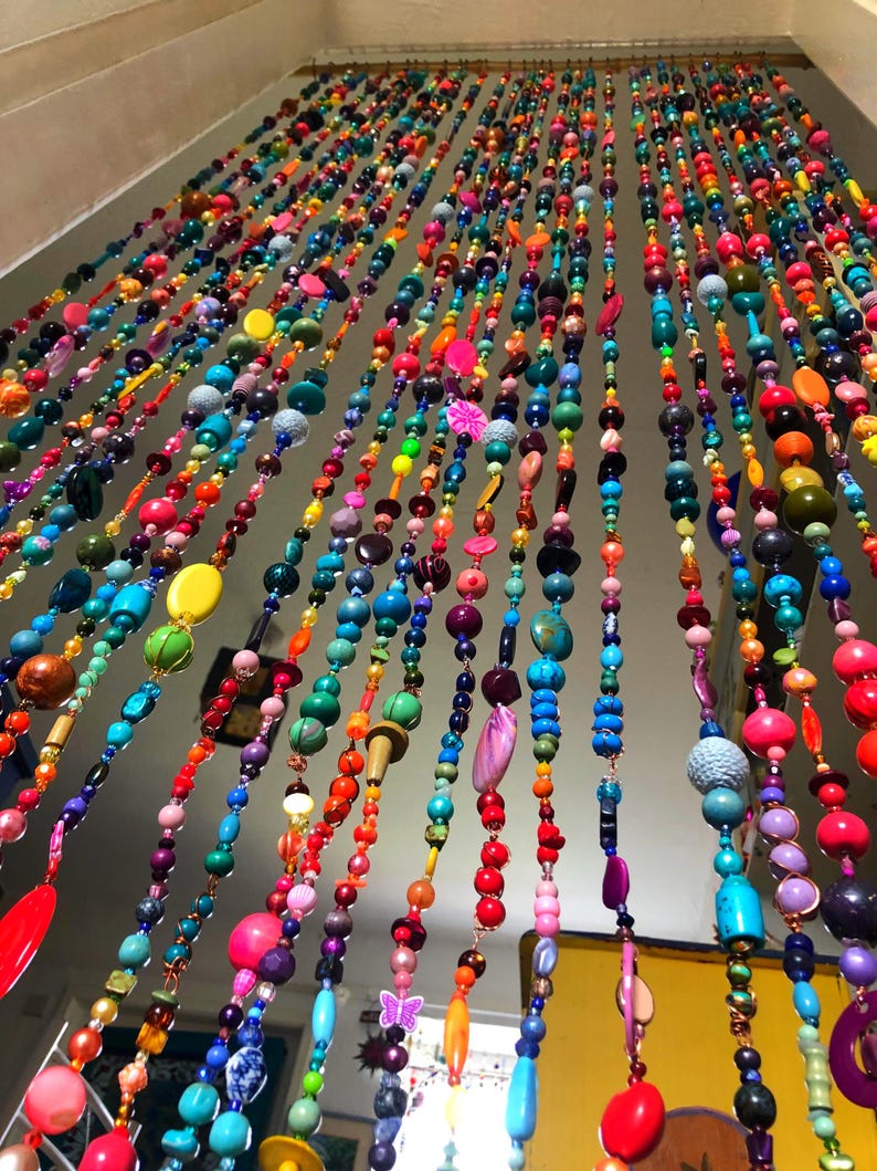 Pu&ograve; includere: Una vibrante tenda di perline multicolore &egrave; appesa al soffitto. La tenda &egrave; composta da numerosi fili, ciascuno adornato con perline in una vasta gamma di colori, tra cui rosso, arancione, giallo, verde, blu e viola. Le perline variano per dimensioni e forma.