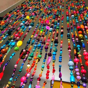 Pu&ograve; includere: Una vivace tenda di perline con fili di perline colorate di varie forme e dimensioni. Le perline sono nelle tonalit&agrave; di rosso, arancione, giallo, verde, blu e viola. La tenda &egrave; appesa a un'asta e crea un'esposizione decorativa e accattivante.