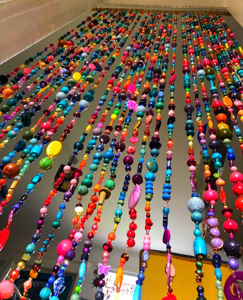 Pu&ograve; includere: Una vivace tenda di perline con fili di perline colorate di varie forme e dimensioni. Le perline sono nelle tonalit&agrave; di rosso, arancione, giallo, verde, blu e viola. La tenda &egrave; appesa a un'asta e crea un'esposizione decorativa e accattivante.
