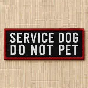 May include: A rectangular patch with the text "SERVICE DOG DO NOT PET" in white block letters on a black background. The patch has a red border and is likely designed to be sewn onto clothing or a harness.