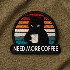 May include: Embroidered patch featuring a black cat holding a coffee mug, set against a sunset design with orange, red, white, and teal stripes. The text "NEED MORE COFFEE" is displayed below the cat.