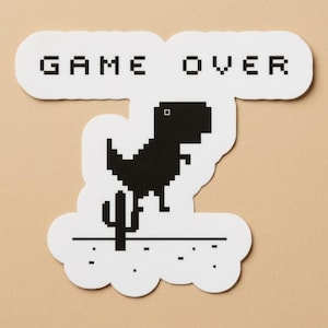May include: A white sticker with a black pixelated dinosaur jumping over a cactus, with the words "GAME OVER" in black pixelated letters above. The sticker has a cloud-like shape.