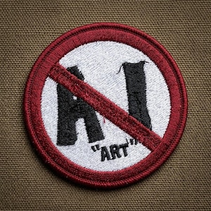 May include: Embroidered patch with a red border and a white center. The patch features a red diagonal line through the black letters "AI" and a black "ART" in quotation marks, all against a tan background.
