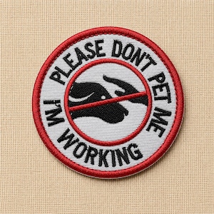 May include: Embroidered patch with the text "PLEASE DON'T PET ME I'M WORKING" in black lettering on a white background, encircled by a red border. The design includes a black silhouette of a dog's head and a hand with a red line through it.