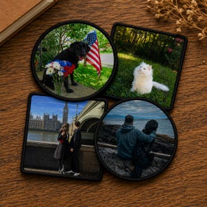 May include: Set of four decorative patches with embroidered black borders. The patches feature images of a black Labrador with an American flag, a white cat in grass, a couple near Big Ben, and a person with a dog by the sea.