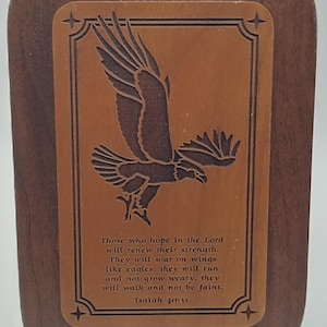 Puede incluir: Placa de madera con un diseño de águila tallada y texto de Isaías 40:31. El águila se representa en vuelo dentro de un marco rectangular, sobre un fondo marrón claro. La placa tiene un borde marrón oscuro.