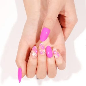 May include: A hand displaying long, oval-shaped, bright pink artificial nails. Some nails have a clear base with small white and pink floral designs. The nails are a vibrant, eye-catching accessory.