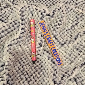 May include: A pink pen with a Hello Kitty design and a black tip. Next to the pen is an orange rectangle with the text "Jenn's Craft Creations" in blue.