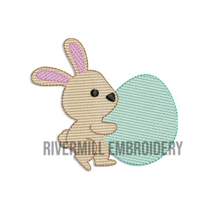 Peut inclure: Motif brodé d'un lapin de dessin animé tenant un œuf de Pâques bleu clair. Le lapin est beige avec l'intérieur des oreilles rose et des yeux noirs. Le texte "RIVERMILL EMBROIDERY" est en dessous.