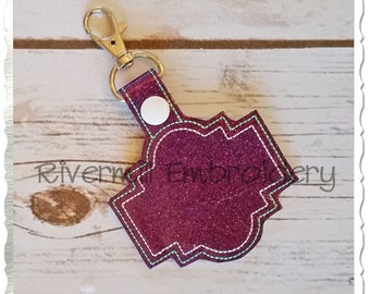 May include: A purple glitter key chain with a white button and a decorative stitched design. The key chain is attached to a silver metal ring.