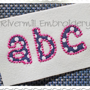 Könnte beinhalten: Gestickte Buchstaben a, b und c in einem marineblauen Stoff mit weißen Punkten. Die Buchstaben sind mit pinkfarbenem Garn umrandet.