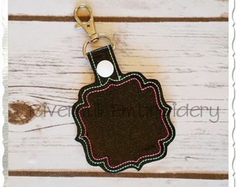 May include: Black key fob with a decorative, scalloped edge. The key fob has a silver-colored clasp and a white button. The edge is stitched with pink and mint green thread. The key fob is a blank slate for personalization.