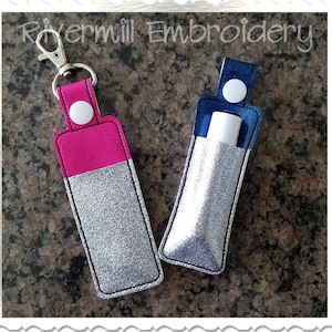 May include: Two silver glitter lip balm holders, one with a pink top and a silver key chain, and the other with a blue top.