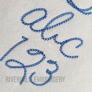 Pu&ograve; includere: Lettere ricamate blu su uno sfondo di tessuto bianco. Le lettere recitano "Love" in un carattere corsivo.