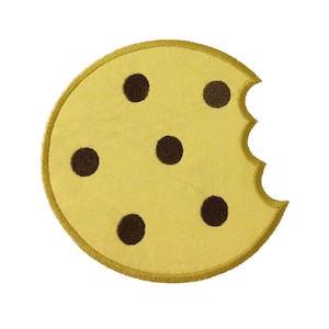 Puede incluir: Una galleta amarilla con un mordisco. La galleta tiene cinco chispas de chocolate marrón.
