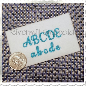 Puede incluir: Primer plano de una tarjeta blanca con las letras "ABCDE" y "abcde" bordadas en hilo turquesa. La tarjeta está sobre una superficie tejida.