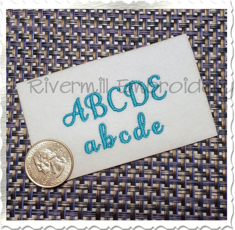 May include: A close-up of a white card with the letters "ABCDE" and "abcde" embroidered in turquoise thread. The card is on a woven surface.