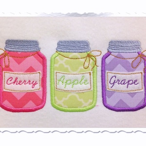 Op de afbeelding: Drie glazen potten met etiketten waarop "Cherry", "Apple" en "Grape" staat. De potten zijn versierd met roze, groene en paarse stof en hebben een zigzagpatroon.