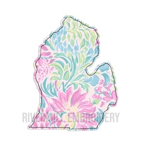 May include: A floral patterned Michigan state outline in pink, blue, and green, with a black stitched border. The text "RIVERSILLY EMBROIDERY" is printed at the bottom. The design is on a white background.