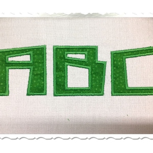 Puede incluir: Letras bordadas verdes "ABC" sobre un fondo de tela blanco.