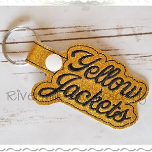 以下が含まれることがあります： イエロー・ジャケットと刺繍された、ゴールドのグリッターキーホルダーです。
