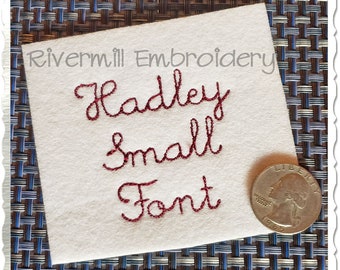 Puede incluir: Primer plano de una tela blanca con el texto "Rivermill Embroidery" y el nombre "Hadley" bordado en una fuente pequeña y cursiva. El texto "Small Font" también está bordado debajo del nombre.