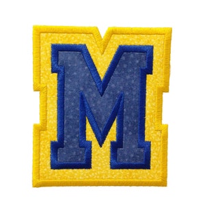May include: A blue felt letter M with a yellow felt border. The letter is stitched with a white thread.