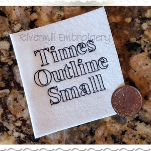 Könnte beinhalten: Weißer Stoff mit schwarzer Stickerei, auf der "Times Outline Small" steht. Eine US-amerikanische Viertel-Dollar-Münze dient als Größenvergleich.