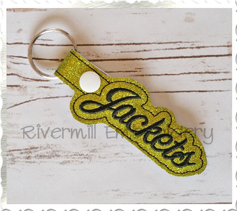 May include: A gold glitter keychain with a black embroidered word "Jackets".