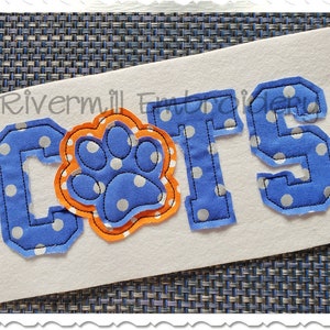 May include: Blue and white fabric letters spelling "CATS" with a blue and white paw print in the center. The letters and paw print have a white polka dot pattern.