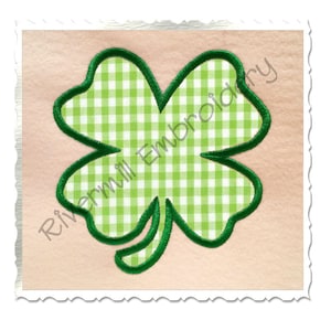 May include: Green four-leaf clover with a gingham pattern inside and a green outline. The clover is on a light pink background. Rivermill Embroidery is written in the bottom left corner.