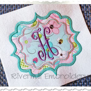 May include: A multi-layered, scalloped frame with a pink, blue, and green floral pattern. The letter "H" is embroidered in purple inside the frame.