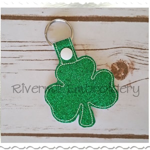May include: A green glitter shamrock keychain with a white button and a silver key ring.