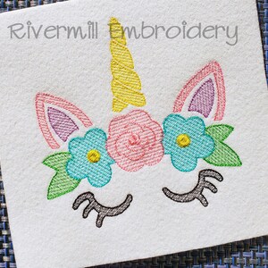 May include: Embroidered unicorn face with a yellow horn, pink and blue flowers, and green leaves. The unicorn has closed eyes with black eyelashes.