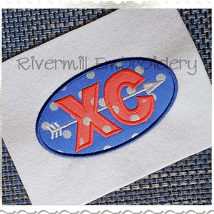 May include: Embroidered patch with the letters "XC" in red with a white outline, and a white arrow pointing to the right. The letters are on a blue background with white polka dots.