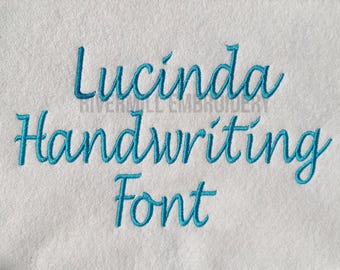 May include: White fabric embroidered with the words "Lucinda Handwriting Font" in teal script. The text is centered and the font appears to be a flowing, cursive style. The words "RIVERMILL EMBROIDERY" are also visible.