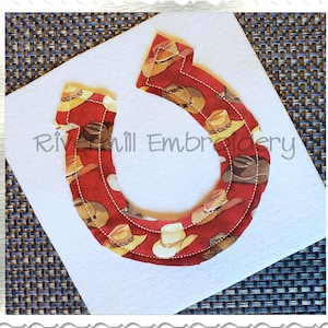 May include: A red, white, and brown horseshoe-shaped applique with a pattern of cowboy hats. The applique is on a white felt background.